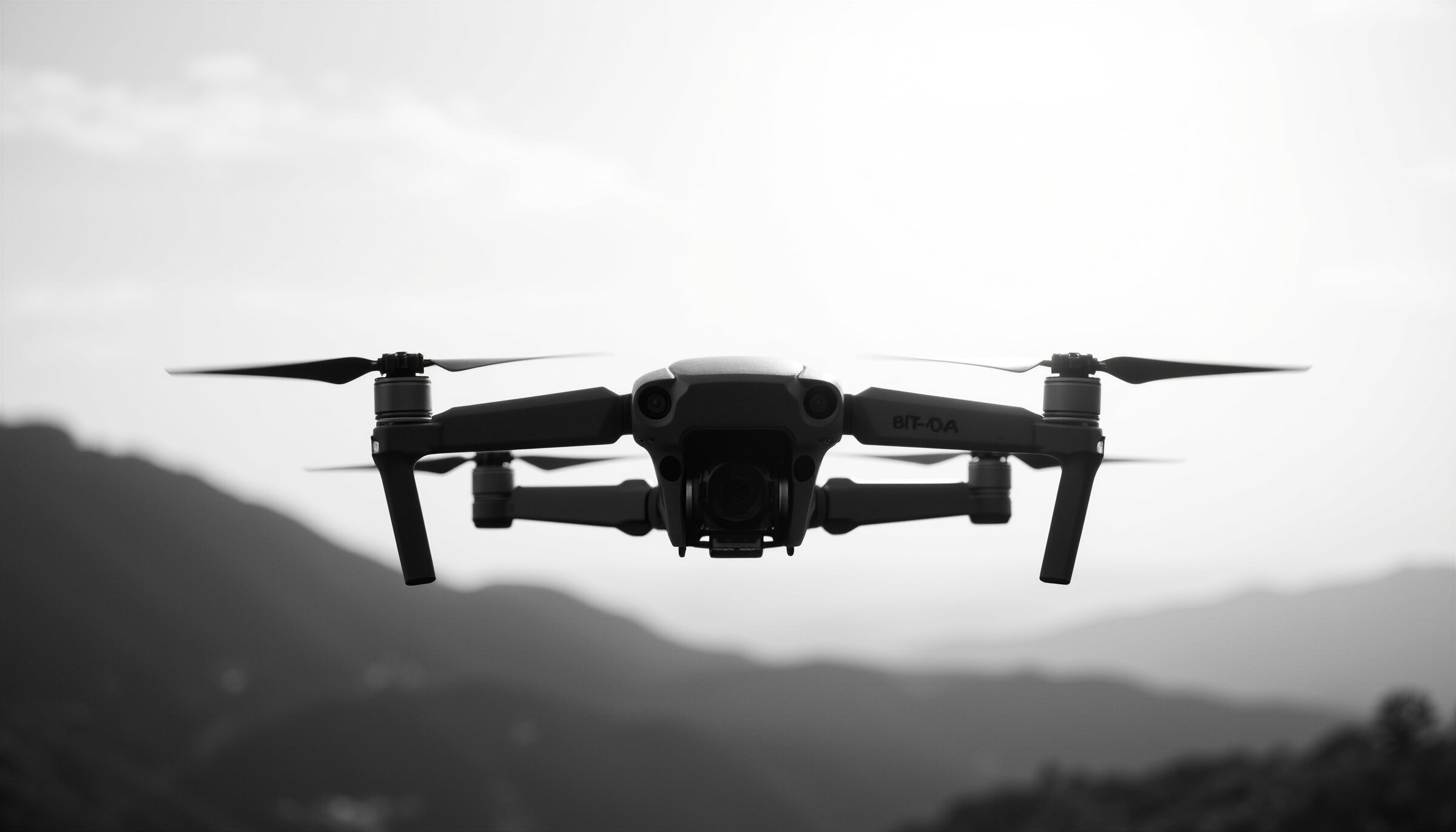 silhouette of a drone in flight against a bright sky over mountain ridges
