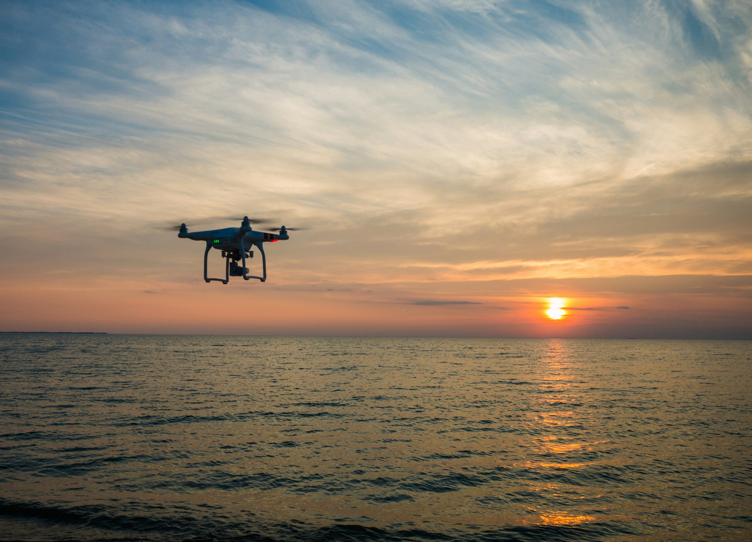 a drone hovering over the ocean at sunset