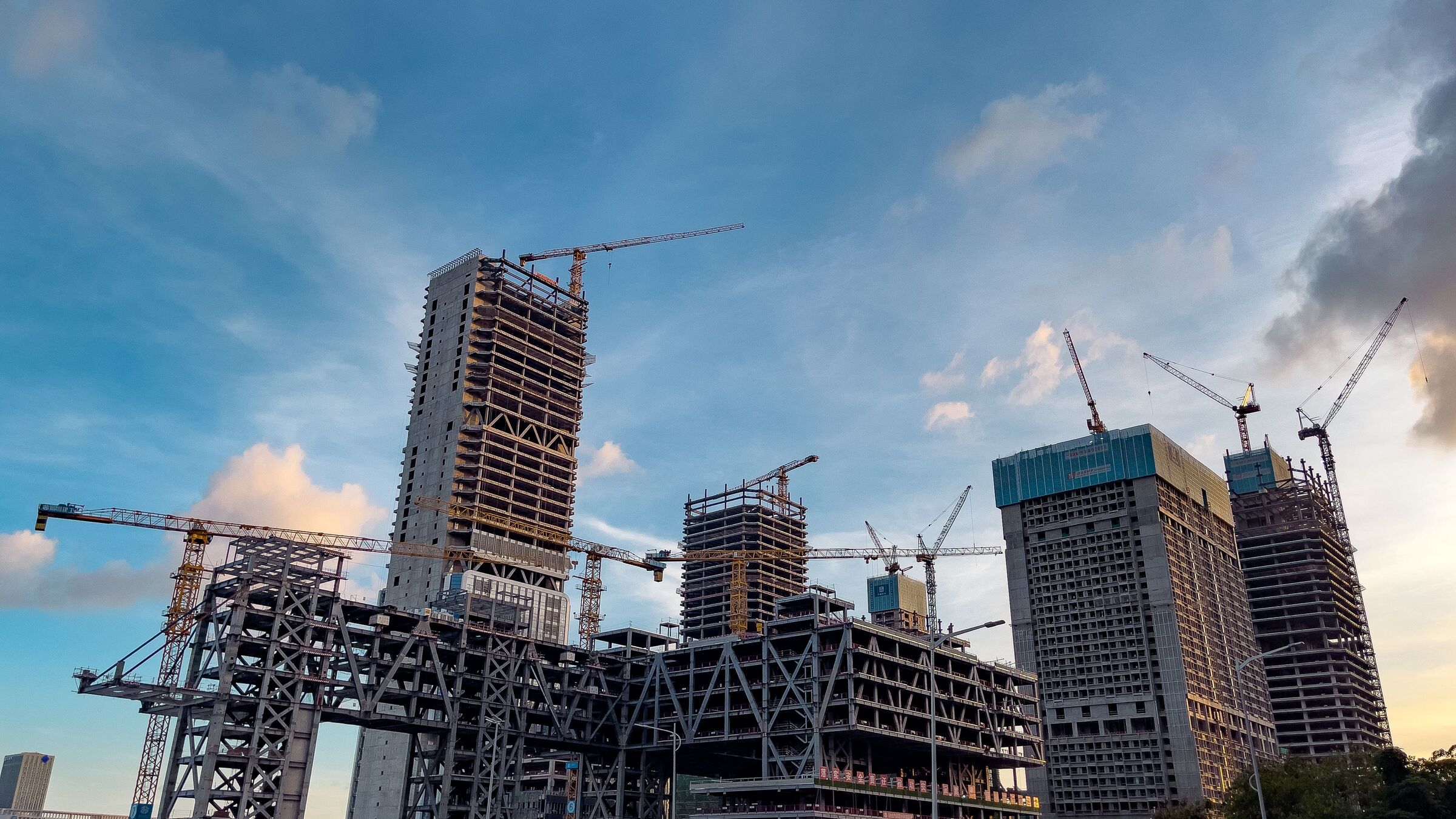 construction cranes over a massive high-rise building project against a dusk sky